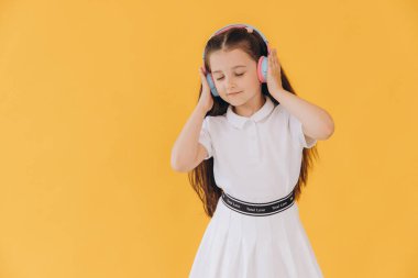 Renkli kulaklıklar takan kız, canlı sarı bir arkaplanda izole edilmiş neşeli ve enerjik bir atmosfer yaratıyor.