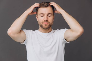 Yakışıklı sakallı adam, stüdyo odasında kafa derisine masaj yapıyor. Güzellik ve bakım konsepti.