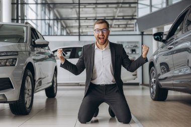 Evet, bu benim yeni arabam! Araba galerisindeki müşteri. Genç mutlu sakallı adam elinde anahtarlarla diz çöktü.