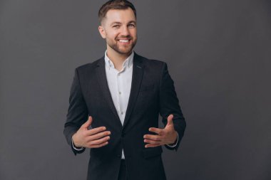 Bin yıllık beyaz iş adamı gri stüdyo arka planında izole edilmiş, resmi takım elbiseli, konuşmacı, diksiyon giymiş, gülümseyen, başarılı bir adam, katlanmış ellerle konuşuyor.