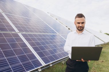 Erkek teknik mühendis dizüstü bilgisayar tutuyor. İnsan güneş enerjisi santralinde işletim ve bakım yapıyor.