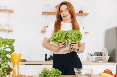 Diş teli takan olgun kaslı kadın evde salata yaprakları tutuyor.