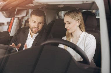 Becerikli araba satıcısı, kadın müşterilere lüks otomobilin içini gösteriyor. Beyaz adam ve kadın içeride oturup konuşuyorlar. Satma ve satın alma kavramı.