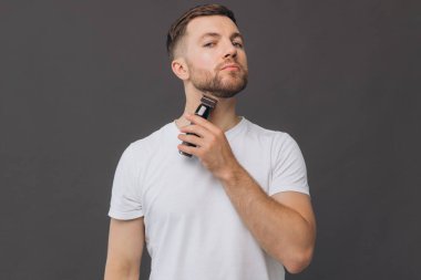 Sakal tıraşı makinesi, portre ya da banyo rutini olan mutlu bir adam, cilt bakımı. Yüz temizleme, yüz bakımı ya da stüdyo çalışanı mutluluğu gri arka planda