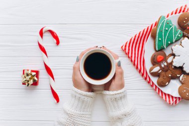 Elinde sıcak kahve, süslemelere karşı şeker kamışı, hediye kutuları ve beyaz ahşap arka planda zencefilli ekmek tabağı tutan bir kadın..