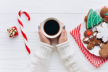 Zencefilli kurabiye, şeker kamışı ve hediyeli bir masanın üzerinde kahve tutan bir çift el. Sıcak bir Noel sabahının, sıcaklığın ve tatil ruhunun mükemmel tasviri..