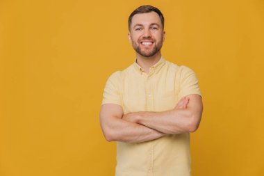 Sağlıklı dişleriyle gülümseyen, sarı gömlekli, sarı arka planda izole edilmiş ve fotokopi çeken sevimli, tıraşsız bir adam.