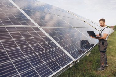 Makinist ya da inşaat işçisi sakallı adam güneş paneli durumunu kontrol etmek için dizüstü bilgisayar kullanıyor. Hücre santrali. Gelişmiş gerçeklik kavramı. Gelecekçi teknoloji