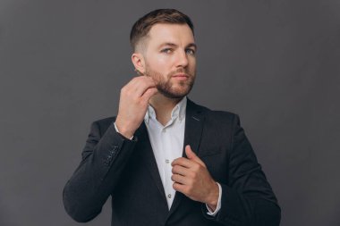 Saçını ve sakalını tarayıp kameraya bakan gri takım elbiseli sakallı iş adamının portresi. Gri stüdyo arkaplanı üzerinde kopya alanı olan bir portre.