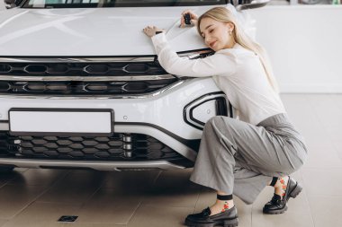 Bayilikte yeni arabasına sarılan olumlu, genç, beyaz bir kadın. Mutlu kadın sonunda uzun zamandır beklenen arabaya kavuştu.