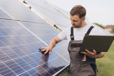 Makinist ya da inşaat işçisi sakallı adam güneş paneli durumunu kontrol etmek için dizüstü bilgisayar kullanıyor. Hücre santrali. Gelişmiş gerçeklik kavramı. Gelecekçi teknoloji