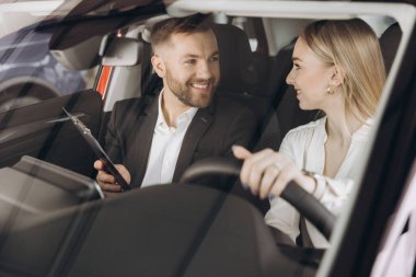 Becerikli araba satıcısı, kadın müşterilere lüks otomobilin içini gösteriyor. Beyaz adam ve kadın içeride oturup konuşuyorlar. Satma ve satın alma kavramı.