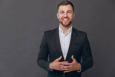 Bin yıllık beyaz iş adamı gri stüdyo arka planında izole edilmiş, resmi takım elbiseli, konuşmacı, diksiyon giymiş, gülümseyen, başarılı bir adam, katlanmış ellerle konuşuyor.