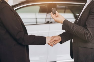 Satıcı ya da menajer araba galerisindeki yeni araba sahibine anahtar verip el sıkışıyor.