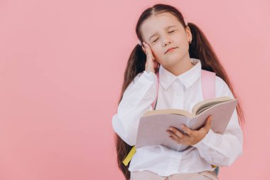 Okul üniforması içinde kitap okuyan güzel bir kız. Elleri başının üstünde ve pembe arka planda yorgun yüzüyle stresli ve hayal kırıklığına uğramış.