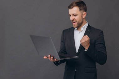 Gri takım elbiseli kendine güvenen işadamının portresi evet derken el ele verip başarılı bir anlaşma yapıyor ve gri arka planda dizüstü bilgisayarla çalışıyor.