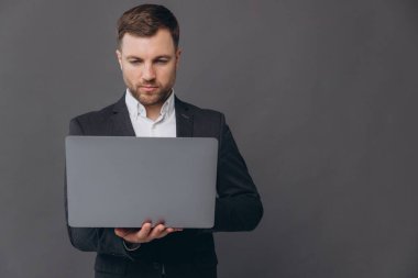 Gri takımlı başarılı ve kendine güvenen iş adamının portresi, dizüstü bilgisayarla çalışıyor, gri arka planda duruyor.