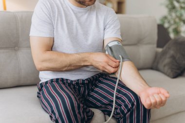 Evdeki kanepede oturan erkek, kan basıncını ölçüyor. Modern tonometre kullanan bir adam stresten kaynaklanan hipertansiyonu hisseder.