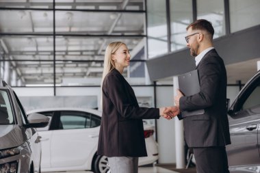 Mutlu kadın bir araba alıyor ve satış temsilcisiyle el sıkışarak işi bitiriyor.