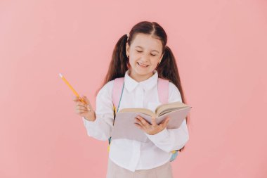 Okul üniformalı, sırt çantalı, kitap okuyan ya da pembe arka planda ödev yazan sevimli bir kız.