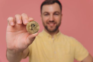 Sakallı adam parmaklarını tutuyor ve altın sikke Bitcoin şifreli para gösteriyor. Elektronik sanal para. Pembe üzerine izole edilmiş kapalı stüdyo çekimi