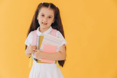 Sarı stüdyo arka planında poz veren mutlu bir okul kızının portresi.