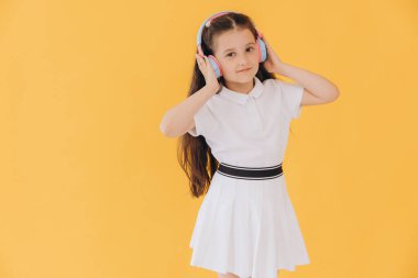 Kablosuz kulaklık takmış, dans eden, sarı duvarda izole bir şekilde müzik dinleyen sevimli beyaz çocuk.