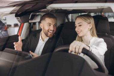 Becerikli araba satıcısı, kadın müşterilere lüks otomobilin içini gösteriyor. Beyaz adam ve kadın içeride oturup konuşuyorlar. Satma ve satın alma kavramı.