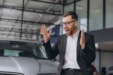 Evet, bu benim yeni arabam! Araba galerisindeki müşteri. Mutlu sakallı adam yeni araba sahibi ellerini kaldırıyor.