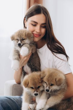Mutlu gülümseyen milenyum kadınlarının portresi. Evdeki kanepede Akita Inu yavrularını kucaklayıp oynuyorlar.