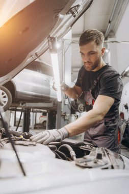 Araba servisi, onarım, bakım ve insan konsepti. Lambalı tamirci atölyede çalışıyor.