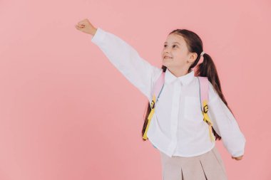 Sırt çantası takan genç bir öğrenci. Kolunu kaldırıyor. Gücünü ve güvenini pembe bir arka planda gösteriyor.