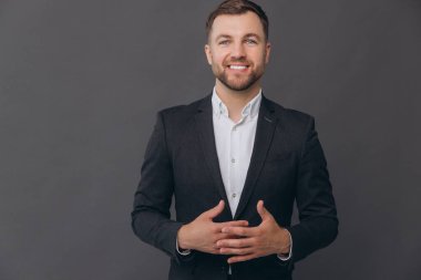 Bin yıllık beyaz iş adamı gri stüdyo arka planında izole edilmiş, resmi takım elbiseli, konuşmacı, diksiyon giymiş, gülümseyen, başarılı bir adam, katlanmış ellerle konuşuyor.