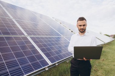 Erkek teknik mühendis dizüstü bilgisayar tutuyor. İnsan güneş enerjisi santralinde işletim ve bakım yapıyor.