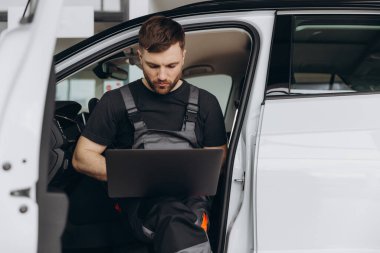 Otomotiv teknisyeni bilgisayarda tanılama yazılımı çalıştırıyor. Tamirci, oto servis garajında aracın tanılama testini yaparken arabada oturup dizüstü bilgisayarla çalışıyor..