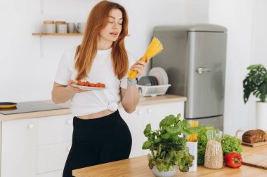 Evde, mutfakta spagetti ve ev yapımı domates sosu pişiren kaslı, güzel bir kadın.