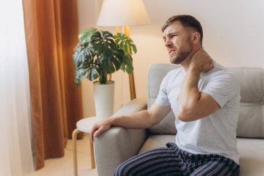 Boyun ağrısı. Kafkasyalı bir adam evdeki oturma odasında boynuna masaj yapıyor. Kemik eklem iltihabı, Sağlık Sorunu Kavramı.