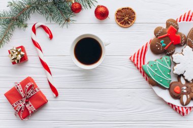 Noel temalı kurabiyelerin hoş bir düzenlemesi bir fincan kahveyle eşleştirilir, etrafları şeker kamışı, çam dalları ve paketlenmiş hediyelerle çevrilidir..