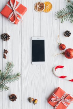 Noel kompozisyonu. Hediyeler, akıllı telefon, çam kozalakları, köknar dalları, şeker, baharatlar ve ahşap beyaz arka plandaki diğer süslemeler. Düz yatış, üst görünüm.