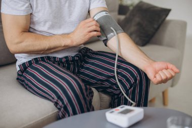 Evdeki kanepede oturan erkek, kan basıncını ölçüyor. Modern tonometre kullanan bir adam stresten kaynaklanan hipertansiyonu hisseder.