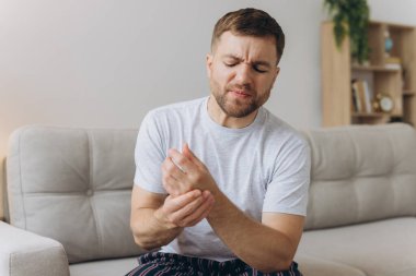 Arthritis symptoms. Man suffering from pain in his hand on sofa at home