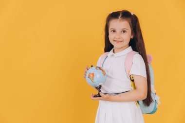 Sarı arka planda dünyadan izole edilmiş beyaz okul üniformalı şirin küçük kız.