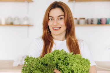 Diş teli takan olgun kaslı kadın evde salata yaprakları tutuyor.