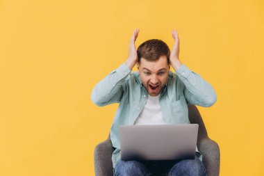 Genç, coşkulu, mutlu, modaya uygun, naneli gömlekli, sandalyede oturan, dizüstü bilgisayarda çalışan, kazanan jest çığlıkları atan, sarı arka plan stüdyosundaki elleri ile başını tutan genç adam..