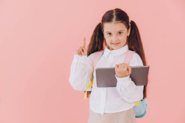 Eğitimde teknolojiyi kucaklayan genç bir ilkokul öğrencisi, canlı pembe bir arka plana karşı dijital tablet kullanıyor.
