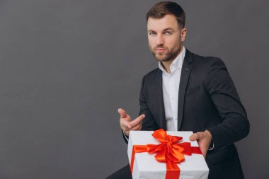 Sakallı mutlu gülen adam elinde bir hediye tutuyor ve gri arka planda, sevgililer gününde, Noel 'de ve yeni yıl konseptinde veriyor.