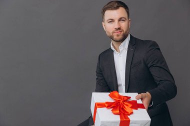 Sakallı mutlu gülen adam elinde bir hediye tutuyor ve gri arka planda, sevgililer gününde, Noel 'de ve yeni yıl konseptinde veriyor.