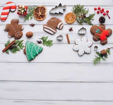 A collection of Christmas cookies, including gingerbread and snowflake shapes, surrounded by holiday decorations like fir branches and spices on a white wooden table. clipart