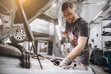 Araba servisi, onarım, bakım ve insan konsepti. Lambalı tamirci atölyede çalışıyor.