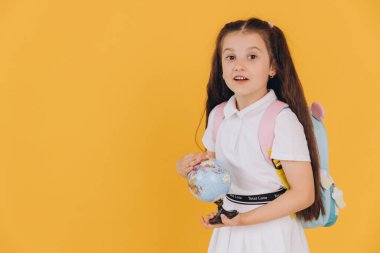 Sarı arka planda dünyadan izole edilmiş beyaz okul üniformalı şirin küçük kız.